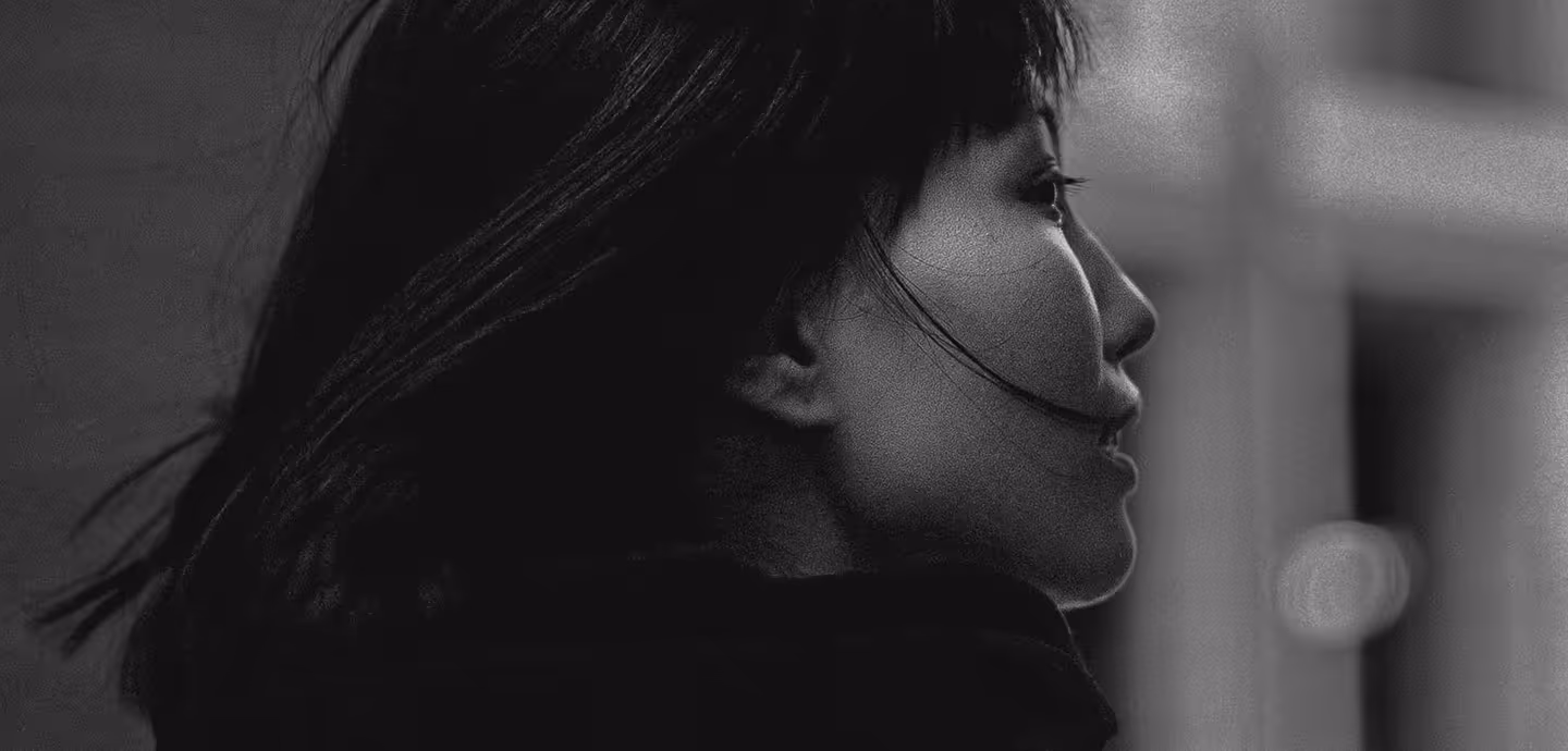 Black-and-white side profile of a woman with shoulder-length hair looking to the right with a blurred urban background.