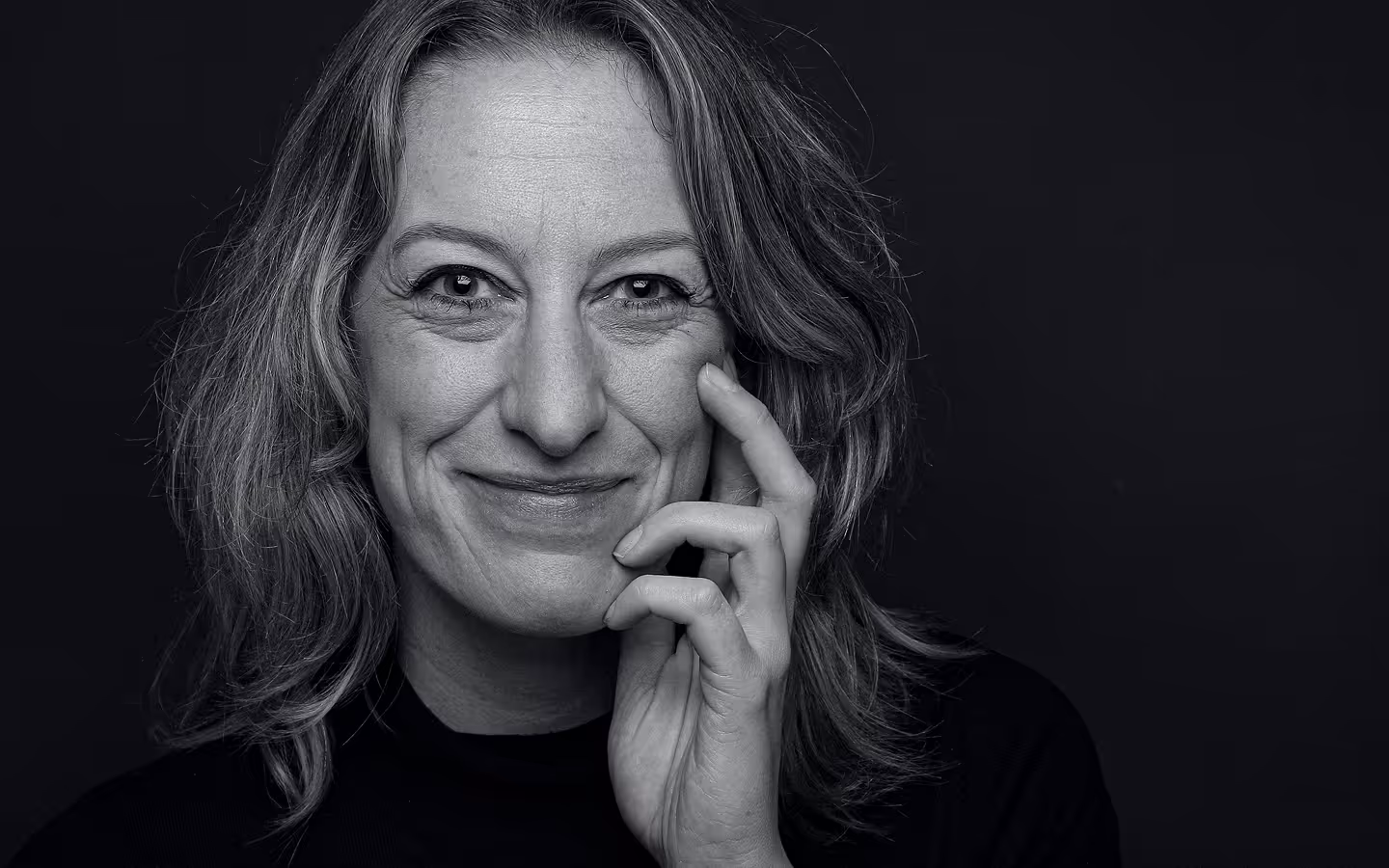 Black and white close-up portrait of a woman smiling softly with her hand gently touching her face.