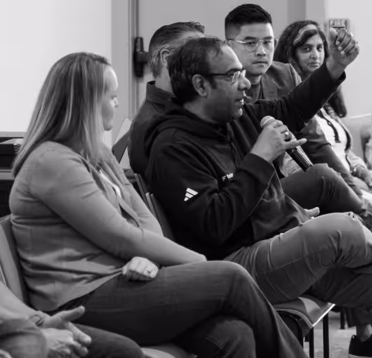 Group of five people sitting in a panel discussion, one man speaking into a microphone and gesturing with his hand.