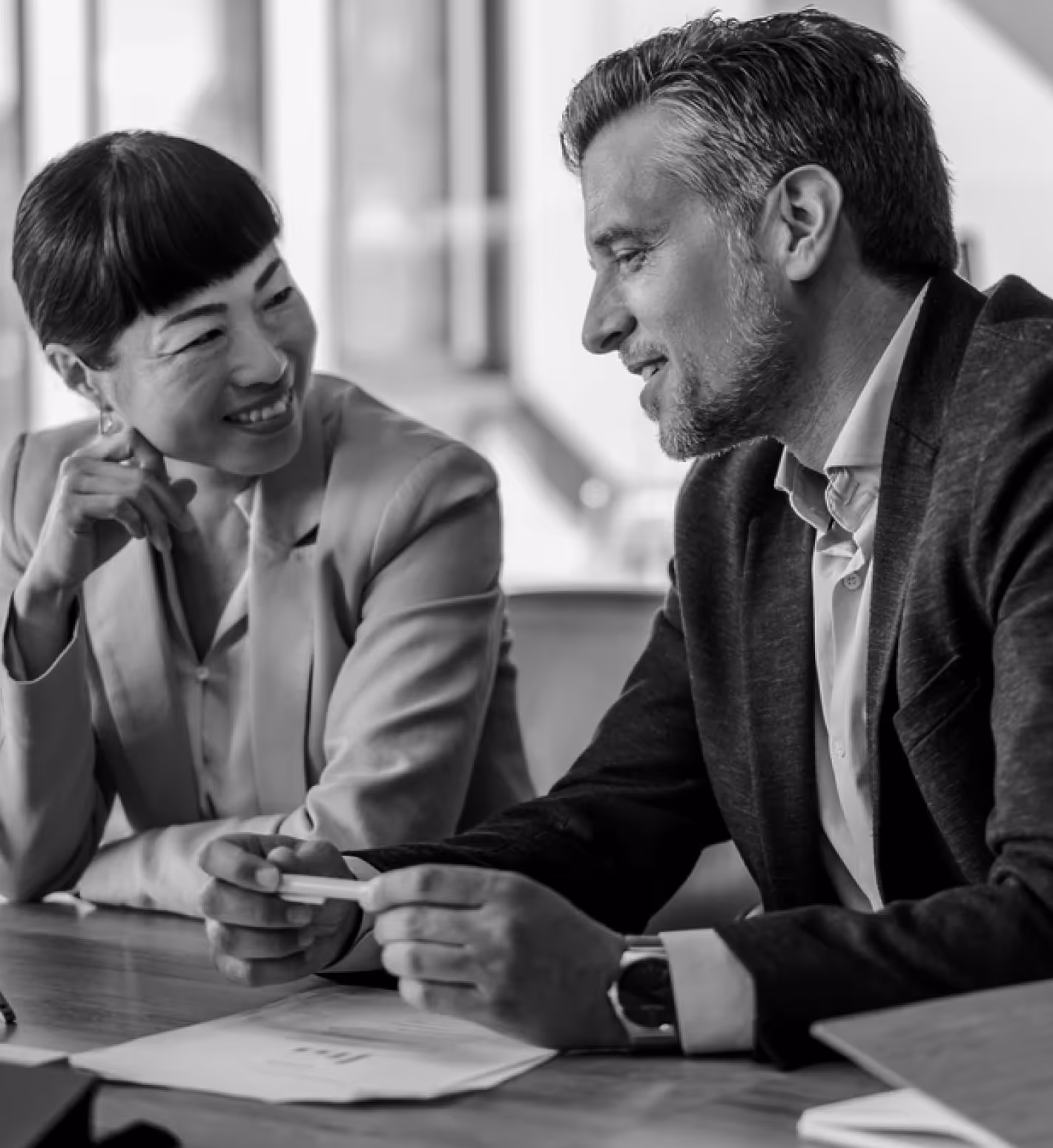Two business professionals smiling and discussing documents at a table in an office.